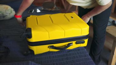 Bir insan sıcak, rahat bir odada düzgün yapılmış bir yatağa parlak sarı bir bavul koyar. Sahne, seyahat hazırlığının ya da evde yerleşmenin özünü yansıtıyor, gelişi, macerayı ve...