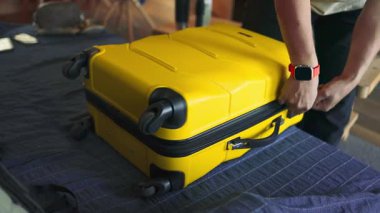 Bir insan düzgün katlanmış kıyafetlerini sarı sert kabuklu bir bavula koyar ve bir yolculuğa hazırlanır. Video, ev içi seyahat rutinini yakalıyor. Giysileri dikkatlice yerleştirirken ellerini gösteriyor.