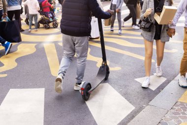 Sokak sahnesinde scooter 'ı olan bir adam ve bir şehir caddesinde bir sürü insan var.
