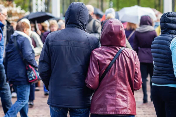 雨の日にレインコートを着て大勢の人々の中を歩くカップルの写真 — ストック写真
