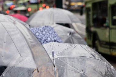 Yağmurlu şehirde şemsiyelerle yürüyen bir kalabalığın resmi.