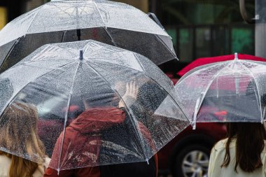 Yağmurlu şehirde bir sokakta bekleyen şemsiyeli insanların resimleri.