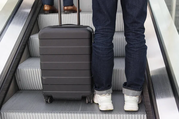 エスカレーターで車輪付きのスーツケースを持った人の足は — ストック写真
