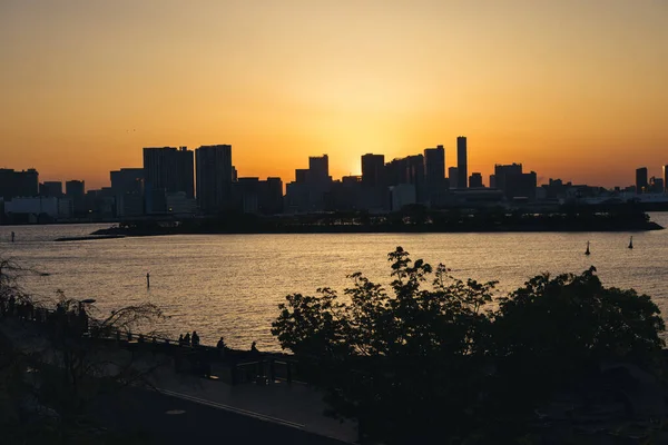 お台場から夕日の東京のスカイラインを望む 前景には誰も知らない人たちのシルエット — ストック写真