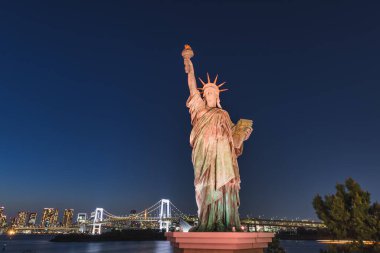 Statue of Liberty at the Odaiba Seaside Park with the Rainbow Bridge in the background, in Tokyo, Japan, at night clipart