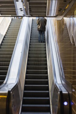 Metro istasyonunda yürüyen merdivendeki bir adamın resmi.