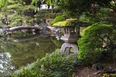 Japonya 'nın Ashikaga kentindeki halka açık bir parkta eski bir fenerin yosun kaplı resmi.
