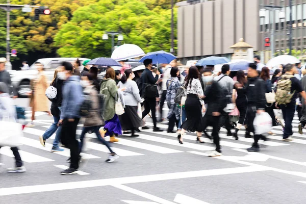 crowds of people with umbrellas crossing a street in Tokyo, Japan, while it is raining