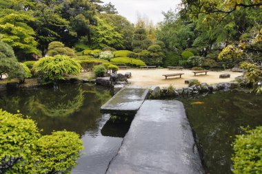 Japonya, Ashikaga 'da bir göletin üzerinde taş köprüsü olan halka açık, geleneksel bir Japon parkının resmi.