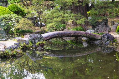 Japonya, Ashikaga 'da bir göletin üzerinde taş köprüsü olan halka açık, geleneksel bir Japon parkının resmi.