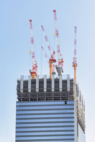 picture of a construction site of a skyscraper with cranes on the top