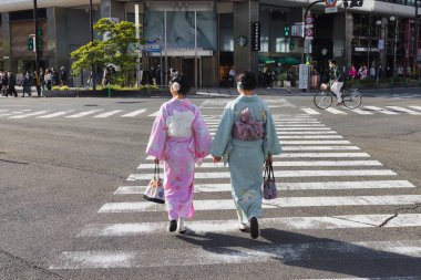 Kyoto, Japonya - 17 Nisan 2023: Geleneksel kimono giymiş kimliği belirsiz genç Japon kadınlar Kyoto istasyonu yakınlarında karşıdan karşıya geçiyorlar. Kimono Japonya 'nın ulusal elbisesidir.
