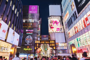 Osaka, Japonya - 13 Nisan 2023: Dotonbori bölgesinde gece vakti, kimliği belirsiz insanlarla alışveriş caddesi ve oyun salonu. Dotonbori, Osakas 'ın başlıca turist ve gece hayatı alanlarından biri olarak bilinir.