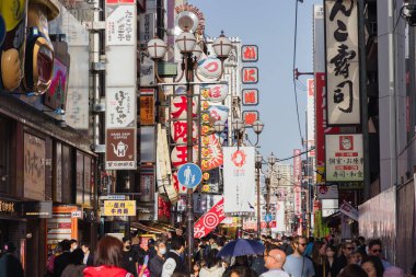 Osaka, Japonya - 13 Nisan 2023: Dotonbori bölgesinde kimliği belirsiz insanlarla alışveriş caddesi. Başlıca turist ve gece hayatı bölgelerinden biri olarak bilinen bölge, Dotonbori kanalı boyunca uzanır.