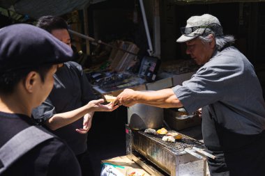 Tokyo, Japonya - 12 Nisan 2023: Tsukiji Balık Pazarı 'nda kimliği belirsiz insanlarla ızgara deniz ürünleri. Bu büyük bir turistik ilgi odağı. 2018 'den önce dünyanın en büyük balık pazarıydı.