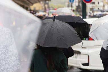 Şehirde yağmurda yürüyen şemsiyeli bir kalabalığın resmi.