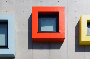 Beton bir cephede modaya uygun renklere sahip benzersiz çerçeveli pencerelerin resmi