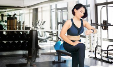 Asyalı kadın spor salonunda spor saati teknolojisini spor süitiyle izlemek için egzersiz yapmaya başladı. 