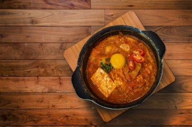 Tofu ve yumurta sarısı ile Kimchi Çorbası Kore Gıda Geleneksel Tarzı konseptinde ahşap masada servis edilir.