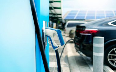 Elektrikli araba şarj istasyonu. Elektrikli araba arka planda güneş enerjisiyle çalışıyor. Yenilenebilir enerji istasyonu kullanan araçlar