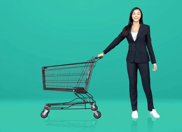 smile asian woman in business suite with shopping cart on green isolated background as studio shot for advertising in marketing theme