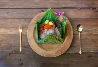 Baharatlı pilav, ızgara domuz eti, ginkgo, tuzlu yumurta, mantar, nilüfer yaprağı ambalajında buharda pişirilmiş Tayland yemeği menüsü ahşap bir tabak ve masada servis edilir..