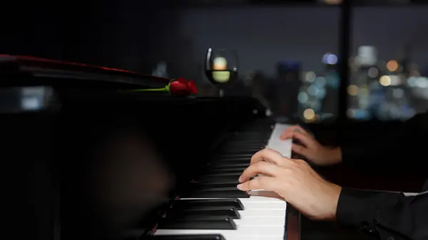 pianist hands playing piano music in dark night with wine and rose in romantic moment