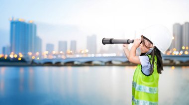 Asyalı çocuk şehrin yaşamını izlemek için teleskopa bakıyor ve gelecek becerileri için güvenli gömlek ve kask takıyor. 