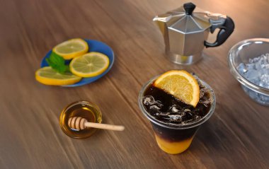 Ballı soğuk portakallı kahve, ahşap masada limon ve buz dilimi.   