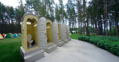 Çadırlar ve açık hava manzaralarıyla çevrili geniş bir kamp alanına yerleştirilmiş taşınabilir tuvalet maceraperest kampçılar ve açık hava meraklıları için idealdir.
