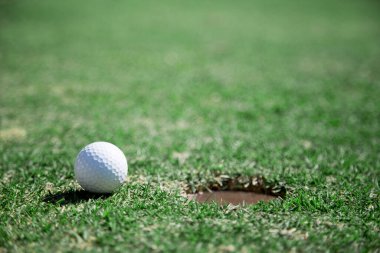 Yeşillik bir golf sahasındaki deliğe düşmek üzere olan bir golf topu başarıyı simgeler ve bir hedefe ulaşır.