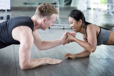 Avrupalı erkek ve Asyalı kadın bir spor salonunda kalas egzersizi yapıyorlar. Partner çalışması