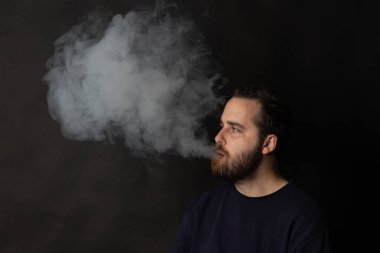 Genç yetişkin bir adam, elektronik sigarasından büyük bir duman bulutu salıyor.