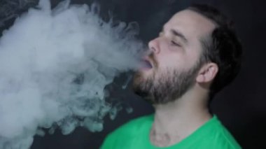Sigara içen adam siyah arka planda duman üflüyor.