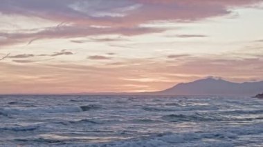 Güneş bir dağ sırasının üzerinde batıyor, okyanus dalgalarının üzerine sıcak bir parıltı saçıyor.