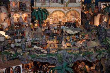 Miniature figurines recreate a lively market scene in a detailed nativity display, showcasing merchants selling various goods clipart