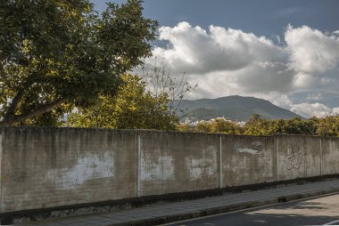 Yıpranmış beton duvar ve grafiti bulutlu bir gökyüzünün altında bir banliyö bölgesini doğadan ayırıyor.