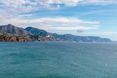 Parlak mavi gökyüzünün altındaki dağlarla çarpıcı bir sahil şeridi.