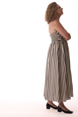 Uzun çizgili bir elbise giyen olgun bir kadının yan görünüşü, çapraz kollarla ayakta durup, derin derin düşüncelere dalmış yukarı bakıyor.