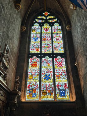 Renkli cam pencerelerden süzülen güneş ışığı tarihi bir kilisedeki çeşitli armaları tasvir ediyor.