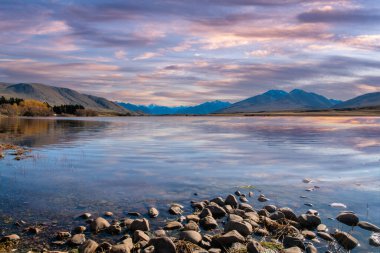 Ön planda bir kaya gölü olan Clearwater Gölü üzerindeki çarpıcı bulutsu renkleri ve yansımaları