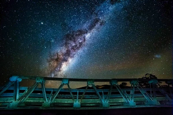 A galaxy of stars and the galactic core bright in the night sky over the steel road bridge
