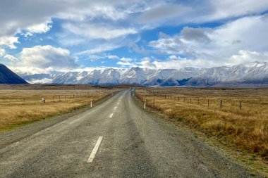 The long country road winding its way through the grass and tussock valley being grazed by farmers on the way to the Ben Ohau snow capped mountain range