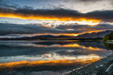 Canlı günbatımı gökyüzü Tekapo Gölü 'nün sakin sularını yansıtıyor