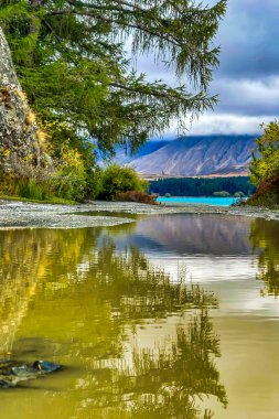 Şiddetli yağmurdan sonra arka planda mavi Tekapo gölü manzarasını yansıtan büyük yağmur birikintileri var.