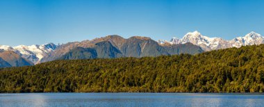 Issız ve ücra bir göl olan Gault, arka planda karla kaplı Güney Alpleriyle çevrili yemyeşil yağmur ormanlarıyla çevrilidir.