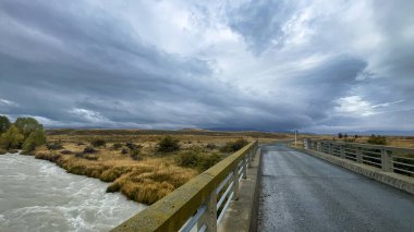 Tekapo Gölü ile Pukaki Gölü arasındaki dolambaçlı dar çakıl yolunda taşan dere kırsal tarım arazisinde.