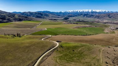 Toprak yol, Lindis Geçidi 'nin yakınındaki kırsal bir vadide karlı dağ sırasına doğru ilerliyor.