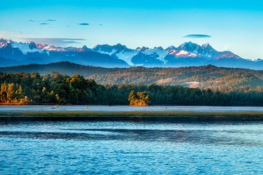 The snow covered Southern alps views from the West Coast Okarito Lagoon at sunrise clipart