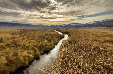 Gün batımında sazlıklardan akan ve dağlara koşan küçük bir su yolu.